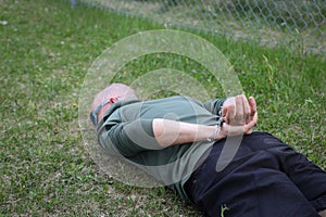 Arrested man in handcuffs face down in the grass of a park