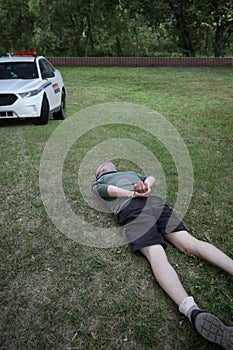Arrested man in handcuffs laying face down on the grass