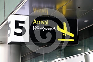 Arrival sign in english and Myanmar language with symbol of the plane landing in yellow on black color at the gate number 5