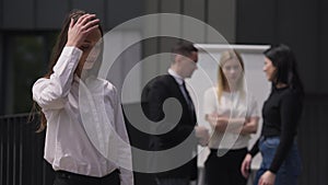 Arrogant burnt out young woman shaking head making facepalm gesture standing on business meeting with coworkers talking