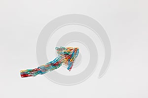 An arrow made from paperclips pointing upwards on a white background, shot from above