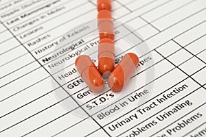 Arrow of orange antibiotic capsules indicates word STDs specified on a sheet of health history. Medications for the treatment of s