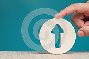 Arrow pointing up on a blue background. Banner with an arrow in a wooden circle in a hand close-up pointing up with copy