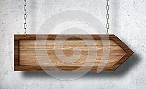 Arrow shaped sign hanging on chains with concrete wall background