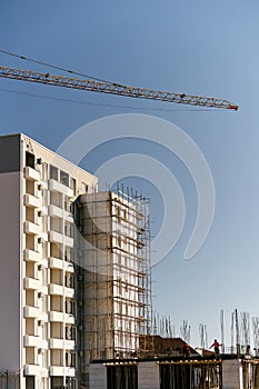 Arrow of a tower crane over the construction of a multi-storey building against the background of the sky. Builders work