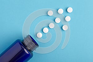 Arrow of white tablets spilling out of package, Close up pills spilling out of pill bottle on blue background. Medicine, medical