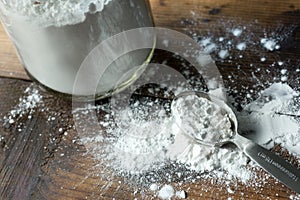 Arrowroot powder in a glass jar, spilled on a rustic wood table. Shown with tablespoon.