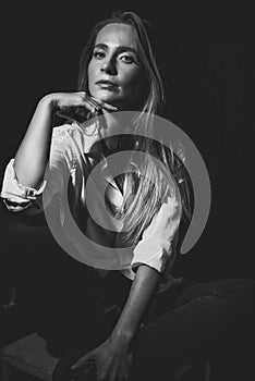 Art black and white portrait of a beautiful girl in a white shirt. Fashionable advertising photo of a young woman on a dark