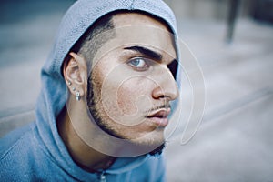 Art conceptual portrait of beautiful middle east brunette man with blue eyes, piercing in blue hoodie