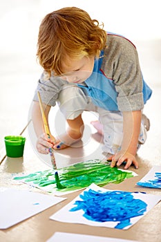 Art, creative and a messy boy painting paper on the floor of his bedroom at home for school homework. Learning, growth