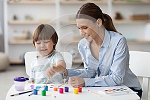 Art development at home. Happy little boy painting with young beautiful mother and laughing, enjoying pastime together