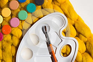 Art equipment: paint, brushes and palette on white and yellow blanket background