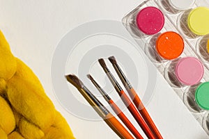 Art equipment: paint and brushes on white paper and yellow blanket background