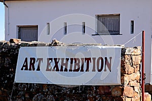 An art exhibition banner hanging on a stone wall in Makhanda, South Africa