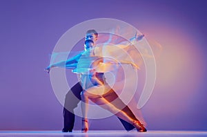 Art in motion. Flexible adorable ballroom dancers in stage attires dancing isolated on purple background in neon mixed