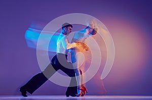 Art in motion. Flexible adorable ballroom dancers in stage attires dancing isolated on purple background in neon mixed