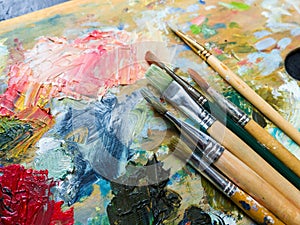 Art paints and brushes lie on the artist`s wooden palette