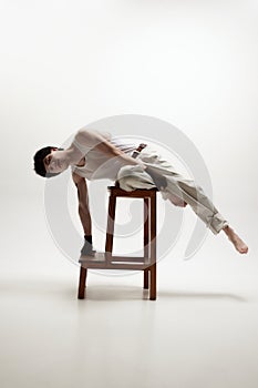 Arte da fotografia. giovane Bello tipo posa pantaloni sdraiarsi sul alto sedie un guarda contro bianco 