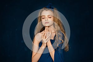 Art Portrait of Beautiful young girl with blonde curly long hair, holding her hands at her face on blue background