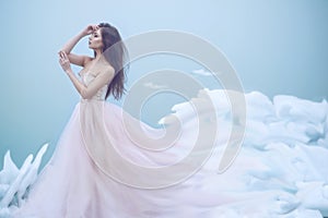 Art portrait of a beautiful young nymph in luxurious strapless ball dress growing into soft clouds