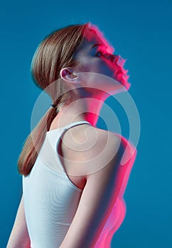 Art portrait of modern young caucasian girl in pink neon light on blue background. Long exposure. Nightlife, youth