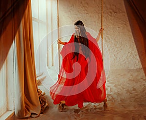 art Portrait real Fantasy girl arabic woman swinging on swing in room of full sand red long silk abaya dress. clothes