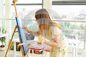 Art school, creativity and leisure concept - student girl or young woman artist with easel, palette and paint brush