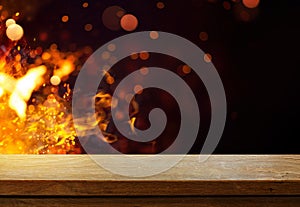 Art Side view of an empty wooden tabletop with orange fire or flames and sparkles on a dark background