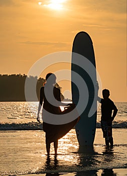 Art Silhouette Smart Asian Couple  Man and Woman, a romantic shot with Standed Surboard on beach with sunset behind them