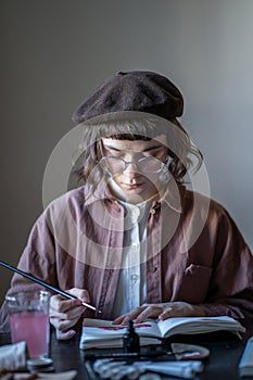 Art student designer illustrator painting sketches in sketchbook sitting at desk in art university.