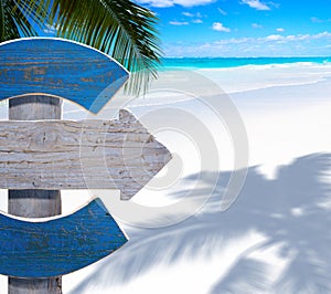 Art wood sign on the sunny tropical sandy beach background with palm trees shadow and blue sea waves