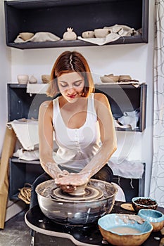 Art workshop, pottery, ceramics. Young master woman working with her hands with a potter`s wheel. Carefully, diligently sculpting