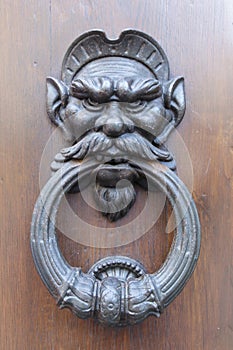 Artful people grimaces as door knockers on antique door in Italy