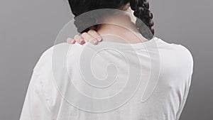 Arthritis and chondrosis. Woman with piggy tails holds her shoulder with her hand, feeling pain. Back view, closeup