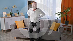 arthritis, unhealthy old man with back pain stands next to sofa, health problems in elderly pensioners