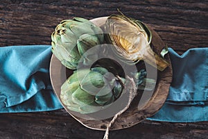 Artichoke close up. Fresh raw organic green Artichokes in a wood plate, closeup. Over wooden table, rustic style