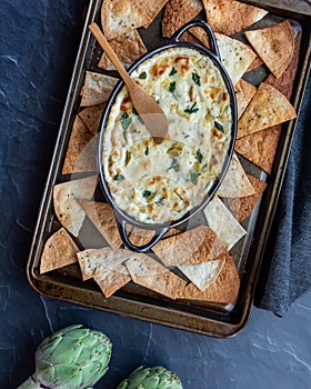 Artichoke dip on a baking sheet with various breads and pita triangles all around.