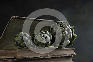 An artichoke and an old book. Artichoke is lying on the book. Dark background. Vintage old book.