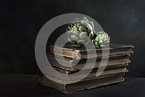 An artichoke and an old book. Artichoke is lying on the book. Dark background. Vintage old book.