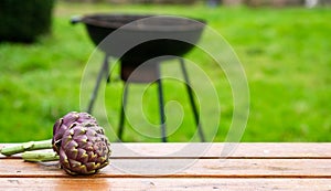 Artichoke on a wooden table outdoors on a blurred grill background. Preparing to cook green grill