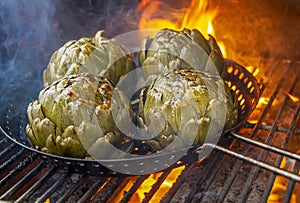 Artichokes charred in pan on BBQ with flames and smoke