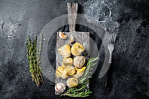 Artichokes hearts marinated with olive oil and herbs, pickled artichoke with garlic on wooden board. Black background