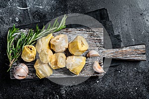 Artichokes hearts marinated with olive oil and herbs, pickled artichoke with garlic on wooden board. Black background