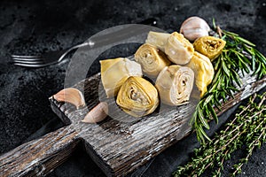 Artichokes hearts marinated with olive oil and herbs, pickled artichoke with garlic on wooden board. Black background
