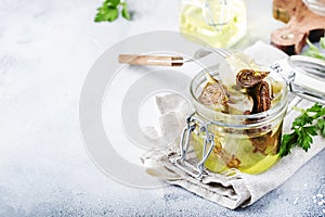Artichokes in olive oil in jar with lemon and herbs on gray kitchen table background, selective focus