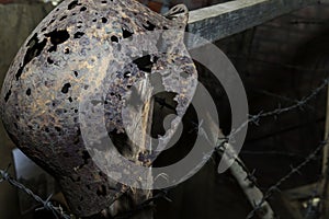 An artifact, a rusty helmet, rests on a barbed wire fence