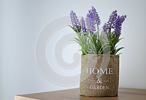 Artificial decorative lavender flowers in a pot with burlap cover and home and garden lettering, standing on a shelf