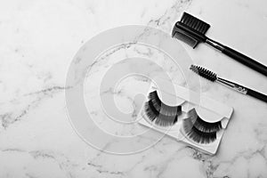 Artificial eyelashes and accessories on marble background, top view