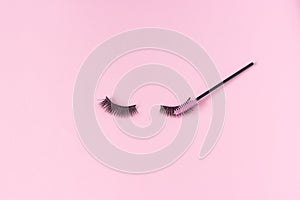 Artificial eyelashes on a pink background and an eyelash brush. The concept of eyelash extensions, makeup