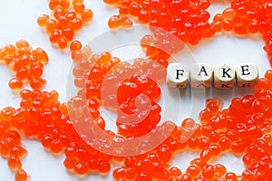 Artificial fake red caviar on a white surface next to the fake sign. The concept of unnatural food, counterfeiting and consumer